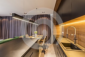 Drapes hanging in modern kitchen interior with black shelves and countertop, wooden table and chairs