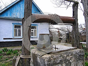 Draw well with metal bucket on chain as rustic water supply. Authentic Russian countryside life. Private peasants house and yard