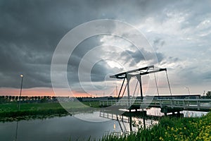 Drawbridge over calm water of a canal in Holland with a dramatic stormy sky in the background