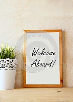 Drawing board with the phrase welcome aboard handwritten over wooden table.