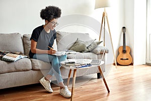 Happy afro american woman, art blogger teaching to draw trough webcamera while sitting on sofa at home photo