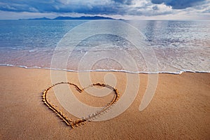 A drawing of a heart on a yellow sand at a beautiful seascape ba