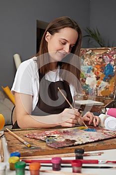 Drawing inspiration from nature. Studio palette for vibrant paintings. Satisfied delighted Caucasian woman painter wearing brown