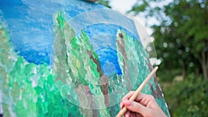 drawing of nature, young woman with a brush and paint draws a picture on canvas in spanking background of green trees