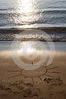 Drawing sun on a sandy beach near to sea. The symbol of resting in sunny day on vacation rest