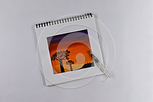 Drawing a watercolor of nature against the background of an evening sunset, sketches on a notebook