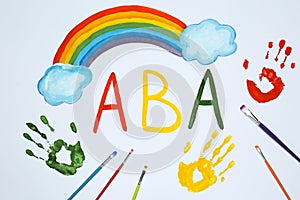 Drawn abbreviation ABA Applied behavior analysis, rainbow, palm prints and paintbrushes on white paper, flat lay