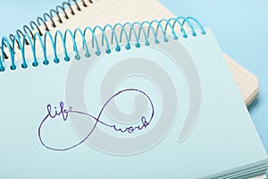 Drawn infinity sign with words Work and Life in notebook on light blue background, closeup. Balance concept