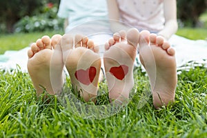 drawn red hearts on the bare feet of two children sitting on the green grass