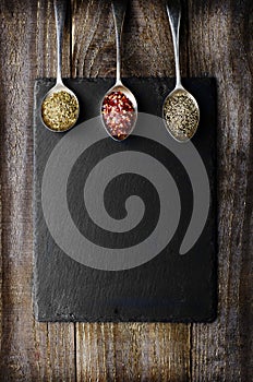 Dray spices on metal spoon on black stone with copy space. Wooden background. Chilli, pepper, marjoram.