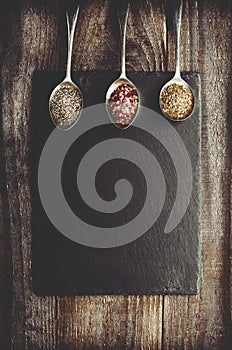 Dray spices on metal spoon on black stone with copy space. Wooden background. Chilli, pepper, marjoram.