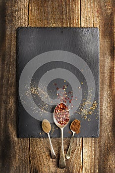 Dray spices on metal spoon on black stone. Wooden background. C