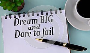 DREAM BIG and DARE TO FAIL - words in a white notebook on a mint background with a cup of coffee