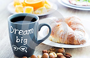 Dream big. Good morning breakfast. Mug of coffee with croissants, nuts and oranges