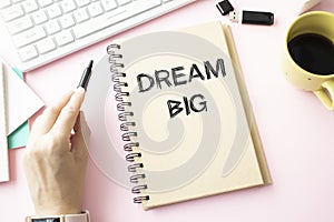 DREAM BIG on notebook on wooden desk with cup and pen