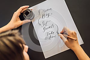Dream big set goals take action. Calligrapher Young Woman writes phrase on white paper. Inscribing ornamental decorated
