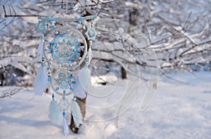 Dream catcher with white and blue feathers and tree branches covered with snow.