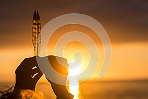 Dream life and hope future concept with close up of hands holding a feather with sunset sunlight in background doing silhouette -