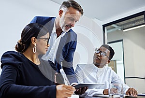 The dream team getting it all done. a group of businesspeople using a digital tablet together in an office.