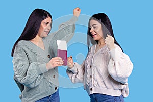 Dream vacation trip. Millennial twin sisters, caucasian girls holding airplane tickets and passports blue background in