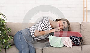 Dream vacation. Woman with suitcase sitting on sofa