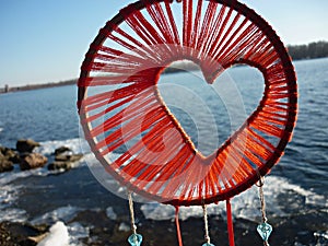 Dreamcatcher in the shape of a heart against the background of the river. Dreamcatcher sunset, mountains, boho-chic, ethnic amulet