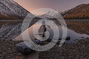 Dreamer. Lonely Man Greets The Dawn Sitting On A Boat Dock On The Shore Of Mountain Lake. Sunrise In Mountains. Old Boat Motor On