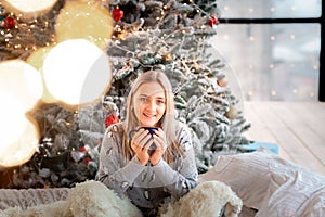 Dreamful cute teen girl near Christmas tree with cup of cacao. Kid wearing pajama dreaming near tree in the morning