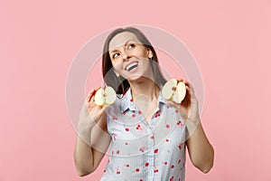 Dreamful pretty young woman in summer clothes looking up holding halfs of fresh ripe apple fruit isolated on pink pastel