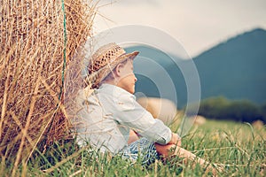 Dreaming boy sitting nea the rolling haystack