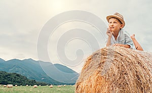 Dreaming boy in straw hat lies on roll haystack