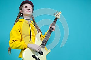 Dreaming Caucasian Teenager Guitar Musician Playing On Yellow Bass Guitar Posing In Fashionable Yellow Hoody Jacket Over Trendy