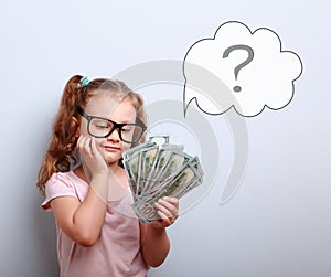 Dreaming cute kid girl in glasses looking on money and thinking