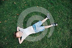 Dreaming cute kid lying on the green grass among fallen leaves