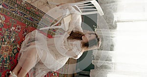 Dreaming elegant woman wearing vintage bridal dress sitting on floor, posing at home in stylish vintage interior