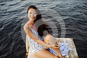 Dreaming girl sitting on the pier of the forest and the river in the background. Sad girl depressed on a bridge by the Sea