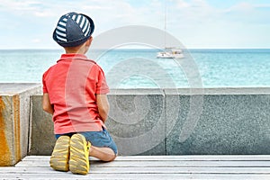 Dreaming little boy with panama looks at yacht sailing sea