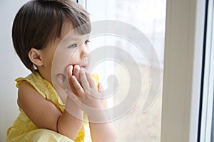 Dreaming little girl portrait leans on elbows on window longing for something. child thinking about pleasing thought