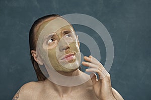 Dreaming man with wet long hair in green clay mask on his face waiting of spa procedures