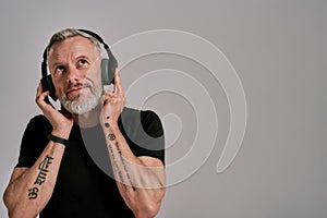 Dreaming. Middle aged muscular man in black t shirt and headphones looking up while listening to music, posing in studio