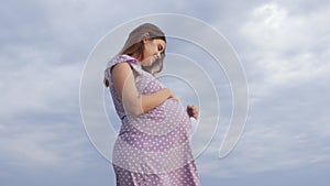 Dreaming pregnant woman in field on background of beautiful clouds