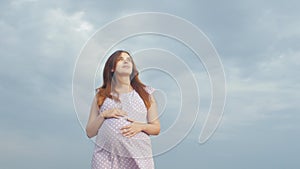 Dreaming pregnant woman in field on background of beautiful clouds