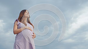 Dreaming pregnant woman in field on background of beautiful clouds