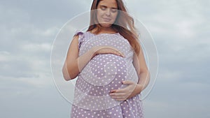 Dreaming pregnant woman in field on background of beautiful clouds