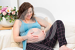 Dreaming pregnant woman watch and touch her beautiful belly resting on the sofa at home