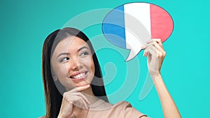Dreaming pretty female holding French speech bubble, fluent foreign language