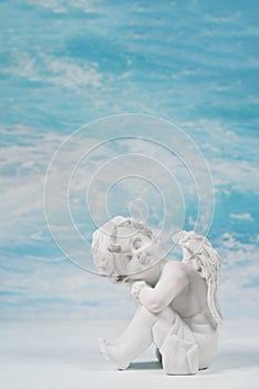 Dreaming or sad white angel on blue heaven background for a condolence card.