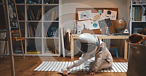 Dreaming of space travel. Happy little child in astronaut suit, helmet playing rocket ship pilot, flying toy in his room