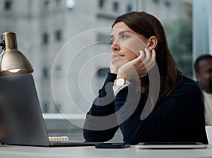 Dreaming about sunny skies. Shot of a young businesswoman looking bored at work.