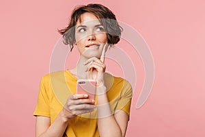 Dreaming young beautiful woman posing isolated over pink wall background using mobile phone